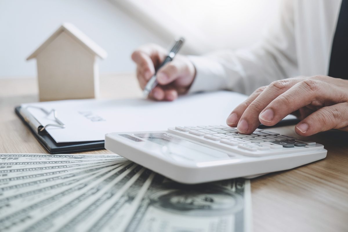 Calcul des frais d’acquisition : calculatrice, billets et maquette de maison sur un bureau